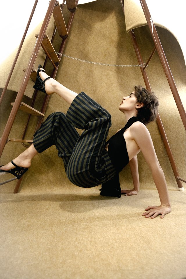 Modelo con top negro y pantalón de rayas junto a una escalera